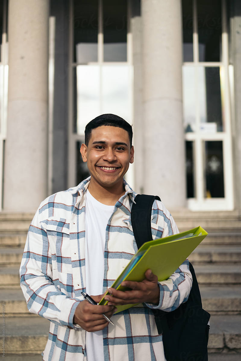 Portrait of a smiling young student with backpack and folder outdoors