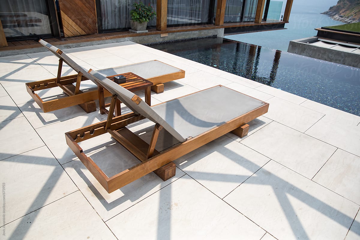 Two outdoor lounge chairs next to a luxurious swimming pool