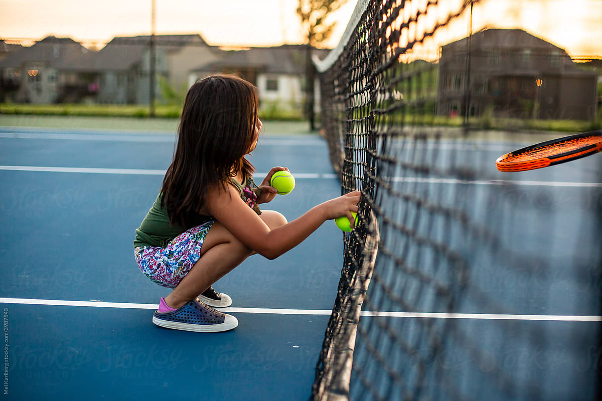 Young girl kneeling next to tennis net