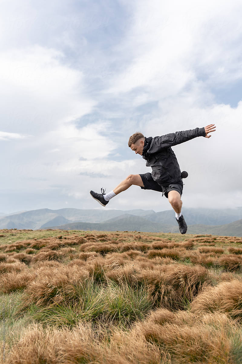 Sportive man jumps above grass field outdoors