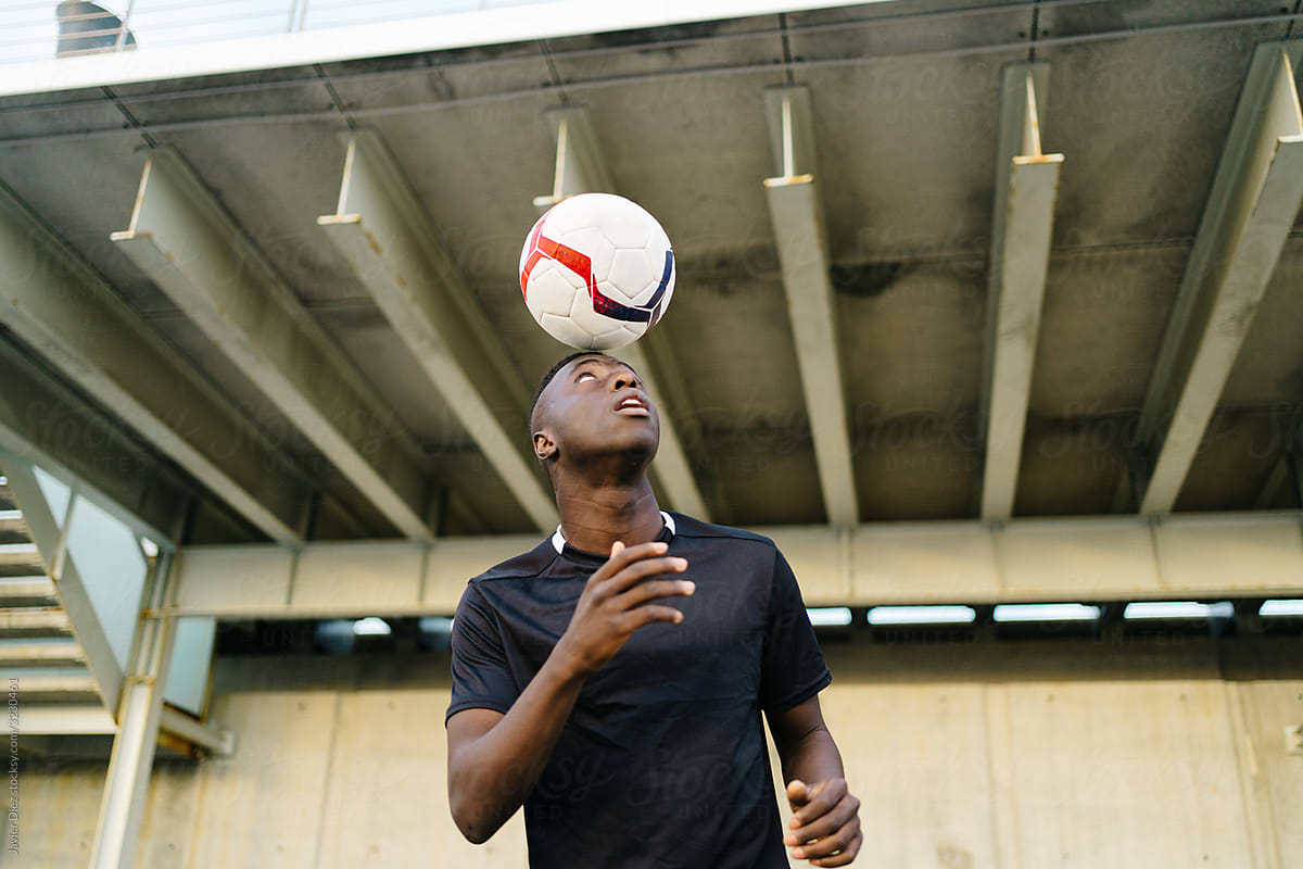 Black sportsman playing football ball on street