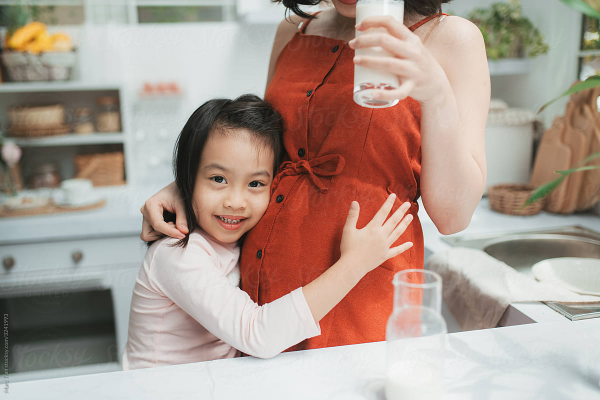 Little Asian girl hugging her pregnant mom