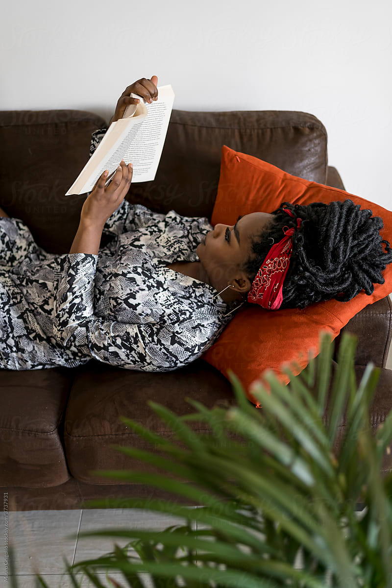 Black woman reading a book on the sofa