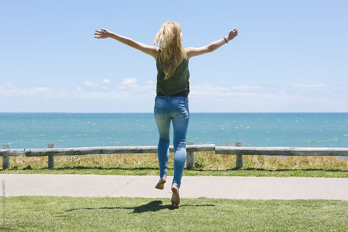 Teenage girl jumping for joy as she runs toward a view of the ocean.