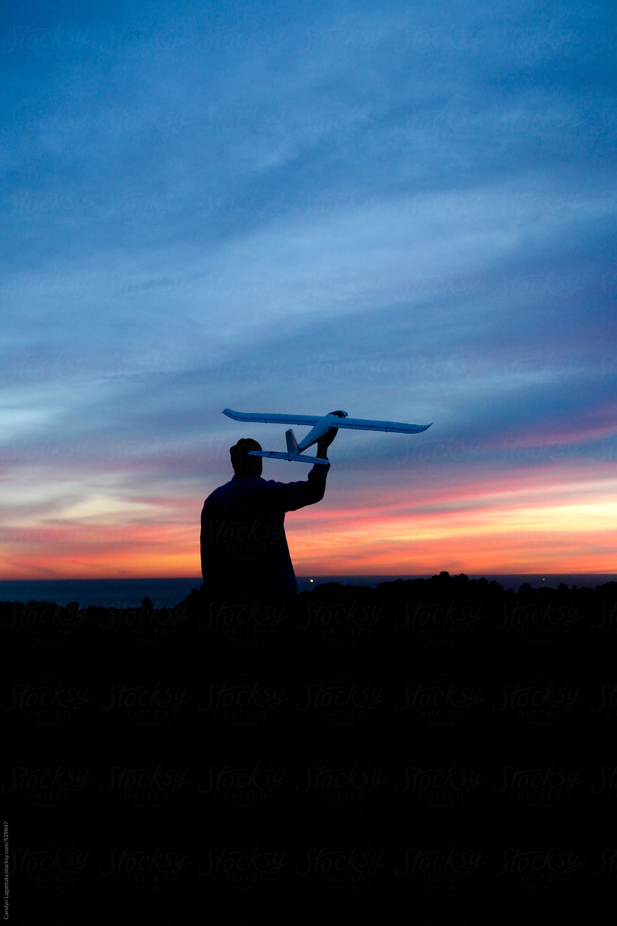 Silhouette of a man holding a large remote control plane at sunset