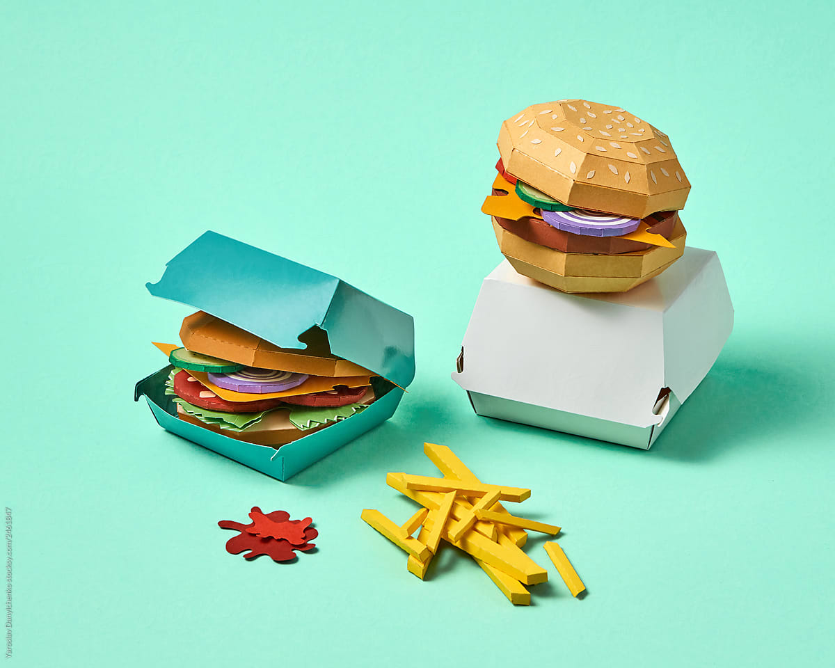 Set of assorted paper handcraft burgers in a cardboard box and fries on a green background with space. Fast snack.