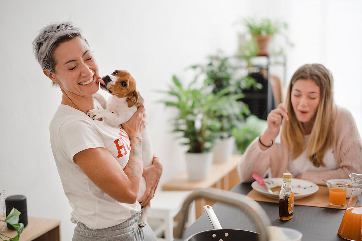 Laughing women with dog at table with breakfast meal