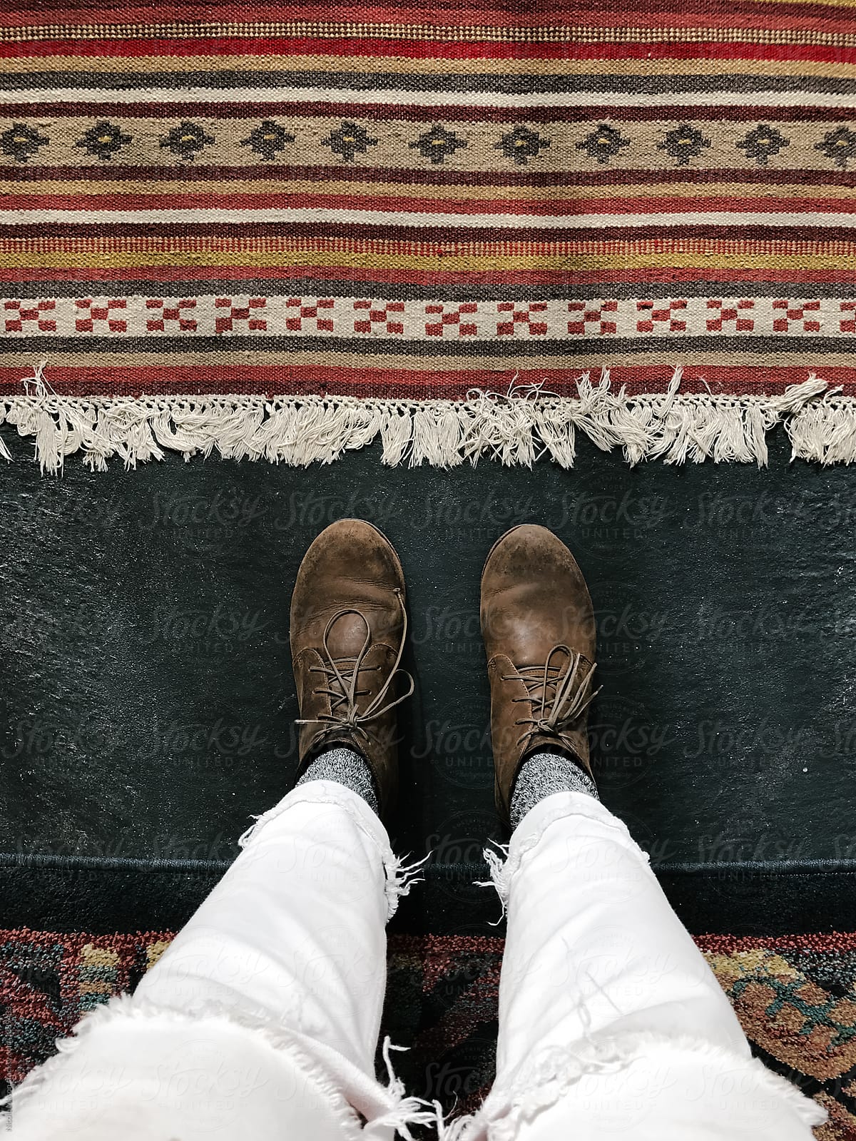 patterned rug on textured floor with person standing in leather shoes