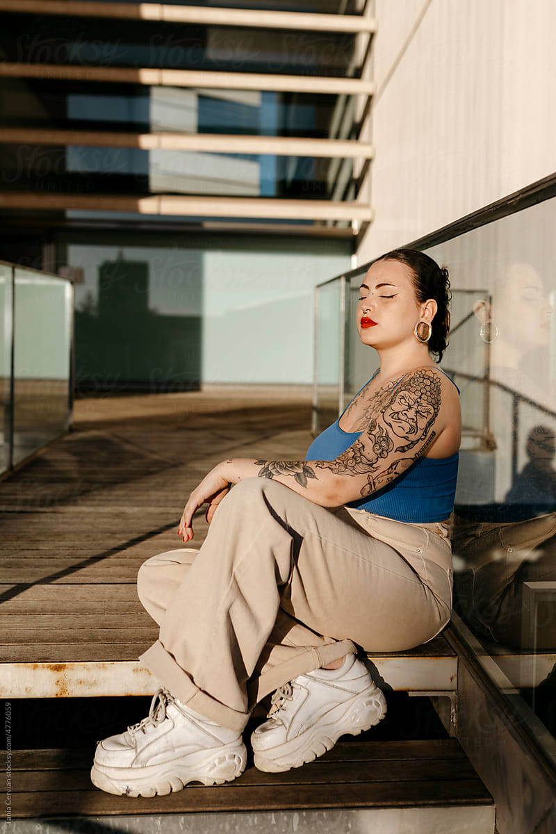 Calm tattooed woman sitting on stairs in city