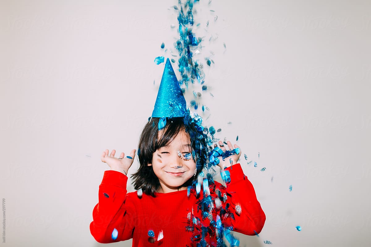 Young mixed race boy in blue party hat plays with confetti