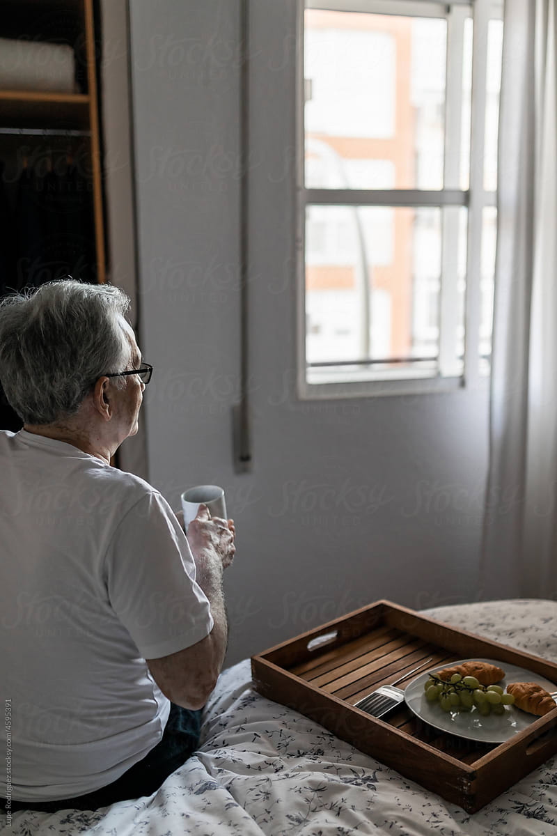 Elderly man looking out the window of his room while having breakfast