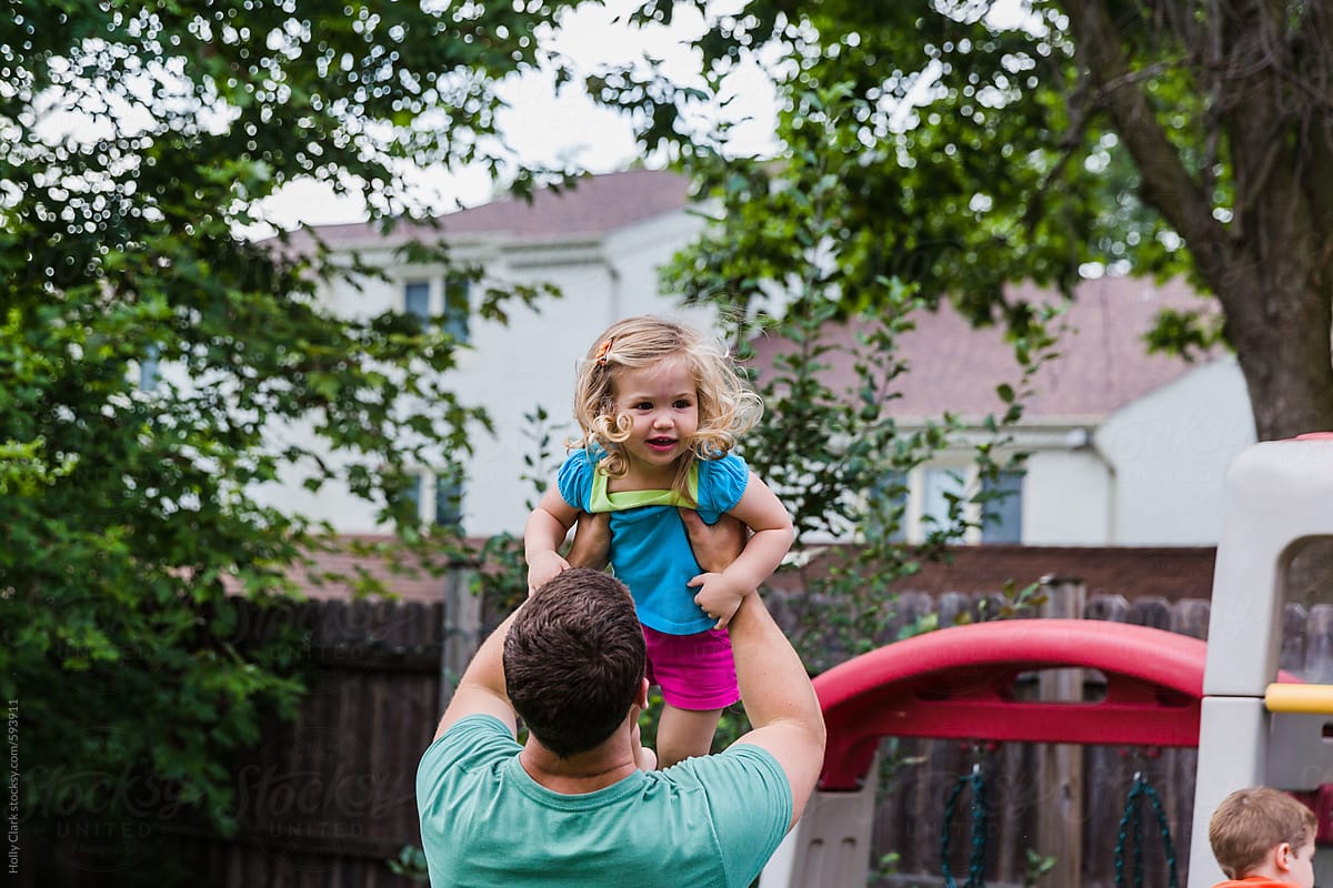 Father playing with daughter in back yard.