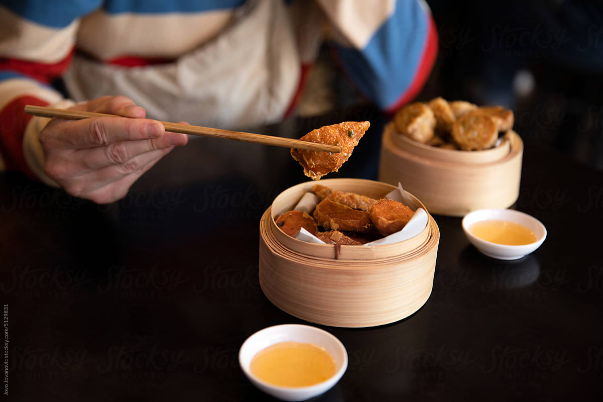 Male hand picking up fried dim sum using chopsticks for eating