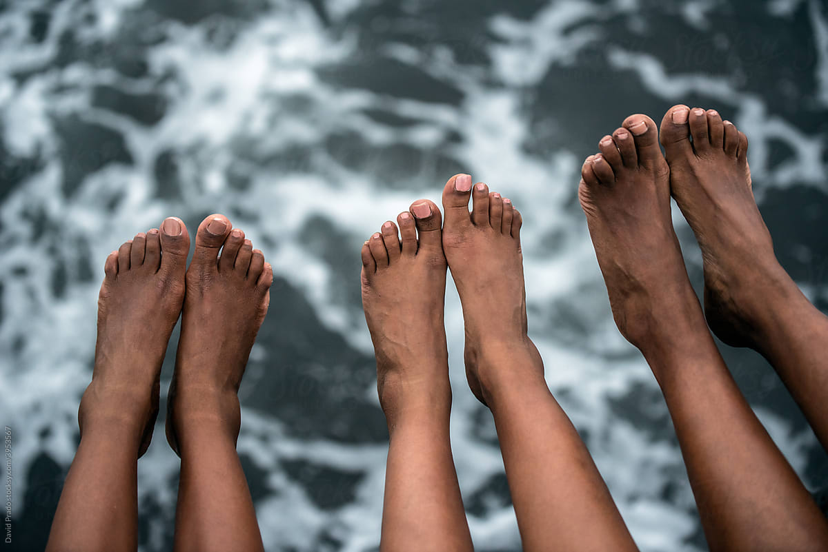 Three sisters feet hanging from a seashore