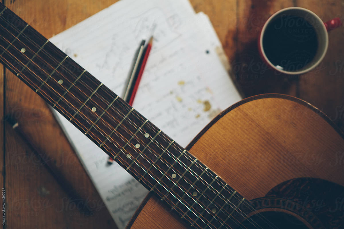 Guitar and coffee cup in the floor next to notepad.