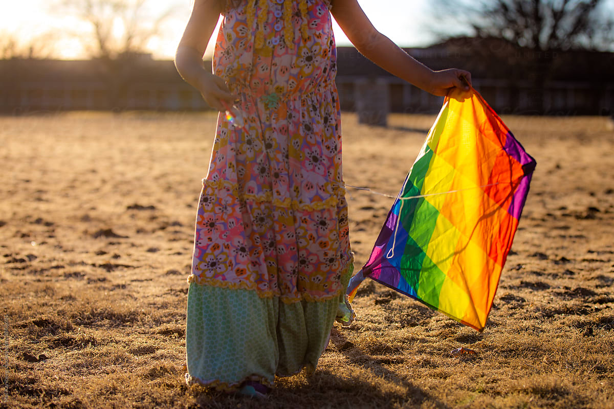 Girl holding rainbow kite at sunset