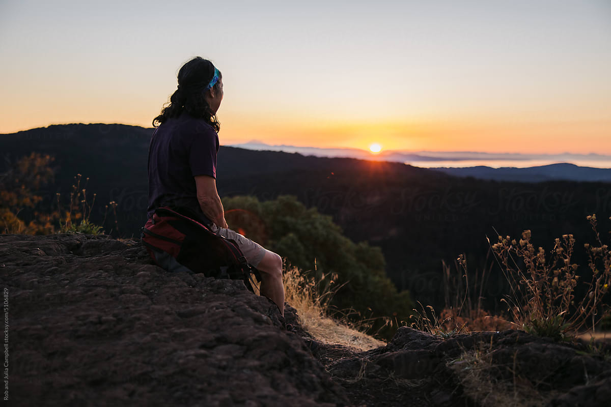 Woman sitting on hilltop watching sunrise.