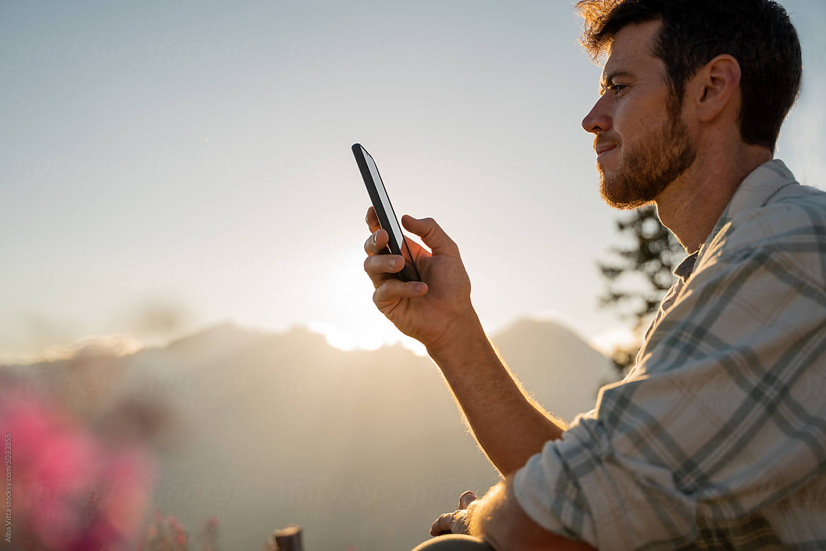 Happy man in the mountain at sunset with phone