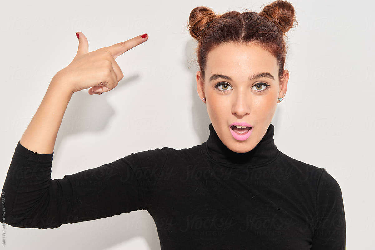 Beautiful girl with buns pointing at her hairstyle.
