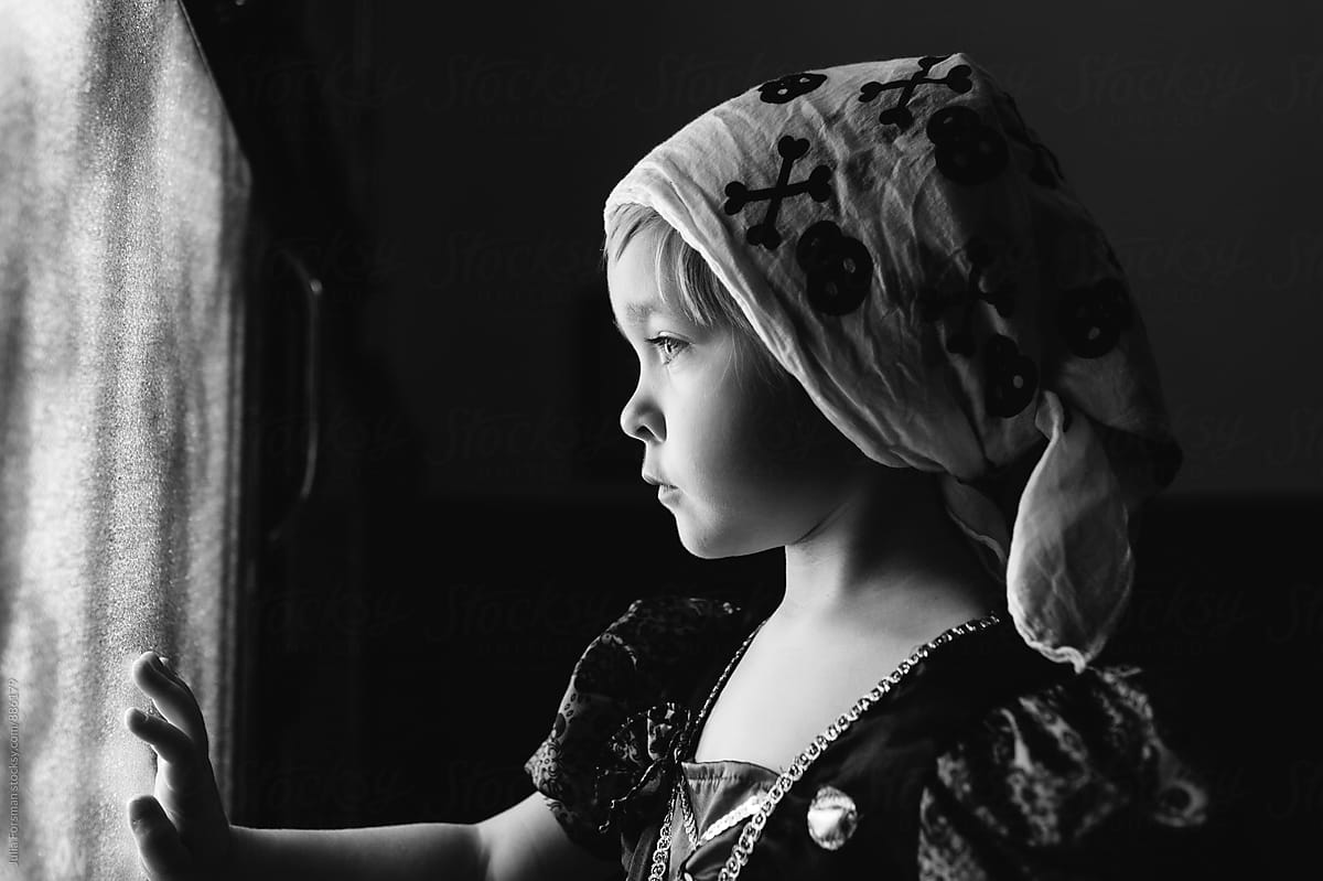 Little girl in pirate scarf looks out of a glass door.