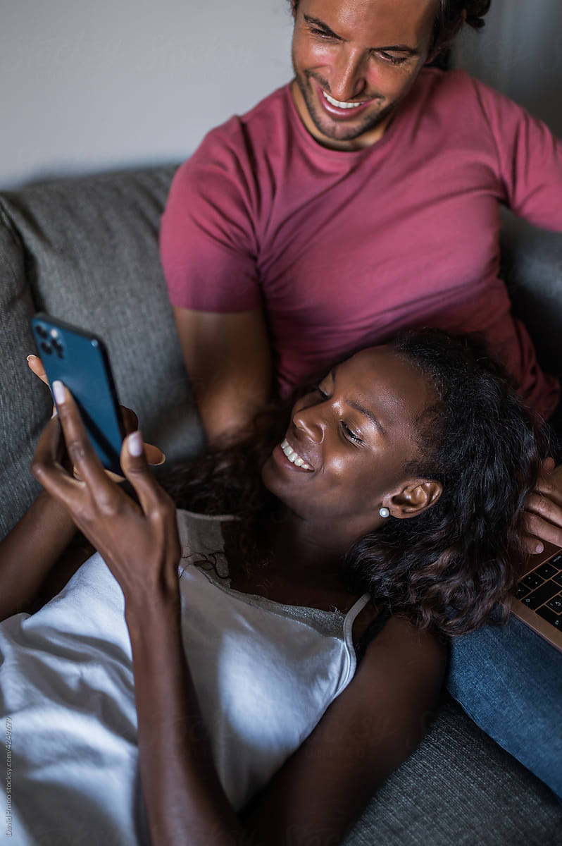 Multiracial couple using devices on couch