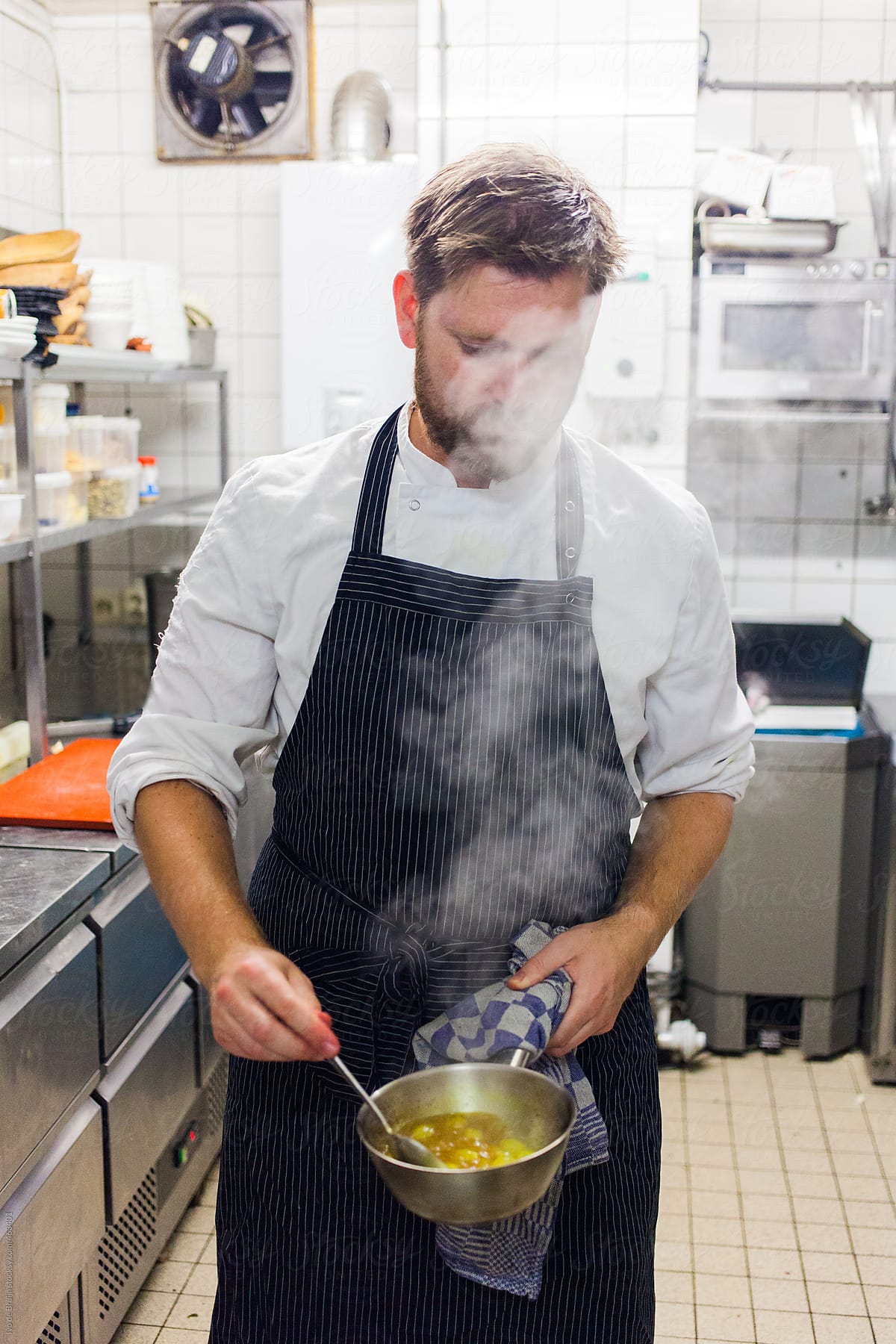 A chef or cook preparing and stirring in a pan while steam is coming out