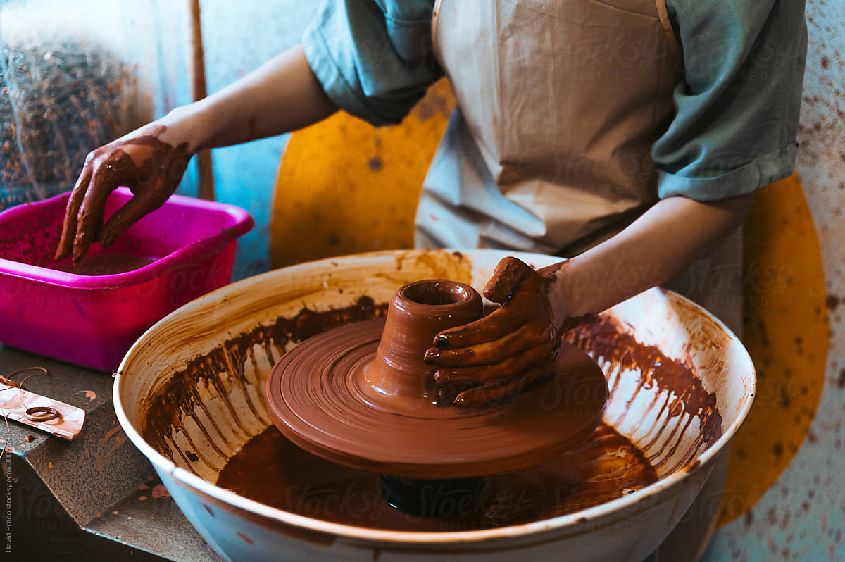 Anonymous young woman ceramist working with pottery wheel in workshop