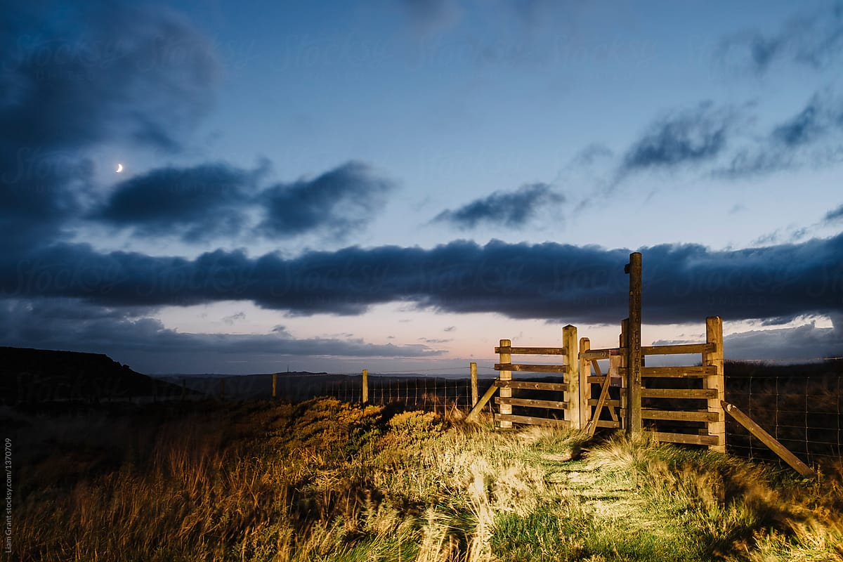 Gate and signpost lit by car headlights at twilight. Derbyshire,