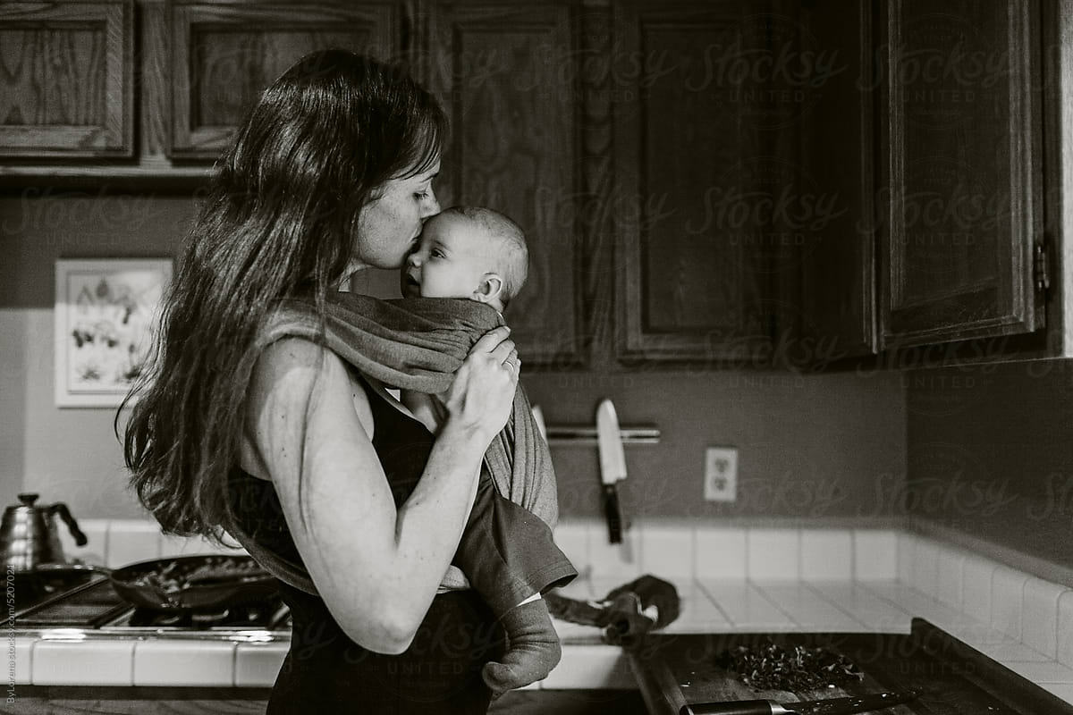 New mom kissing baby while cooking at kitchen