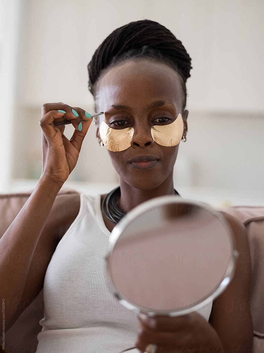 Black woman plucking eyebrows with tweezers