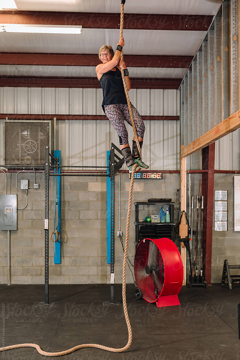 Senior woman climbs rope at gym