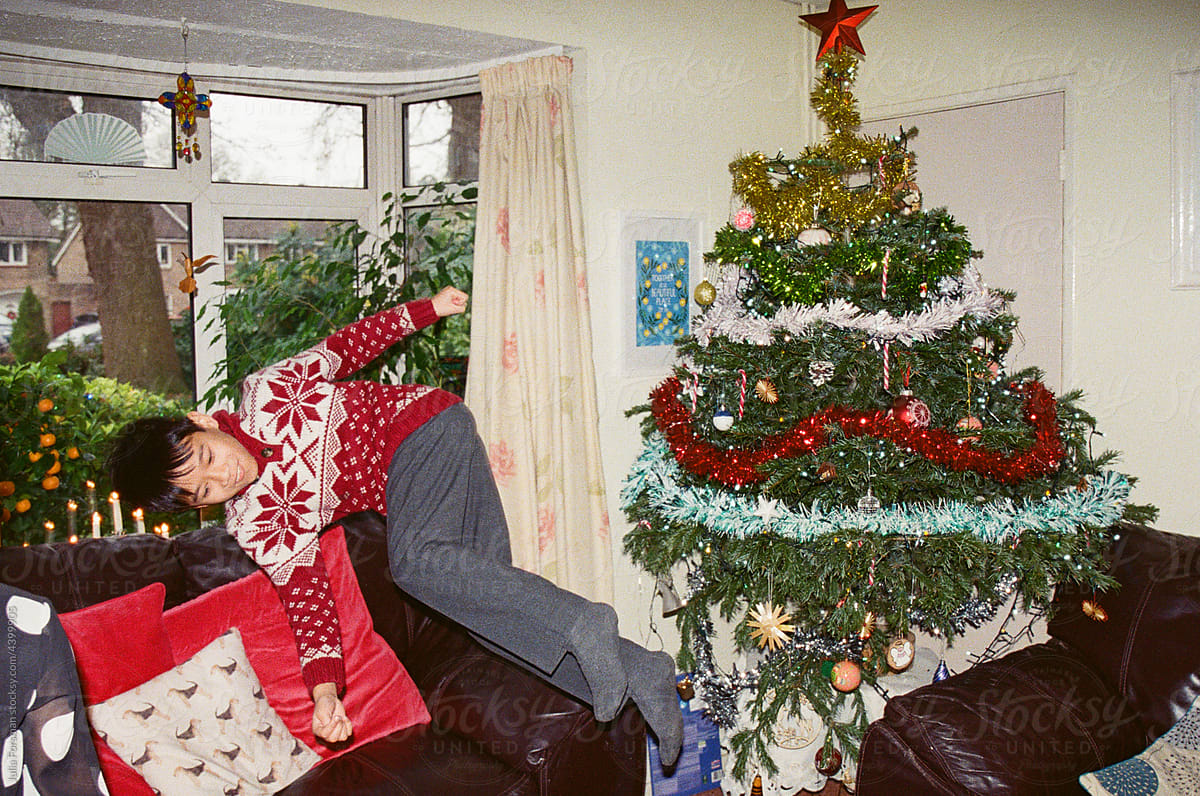 Boy leaps across room with Christmas tree