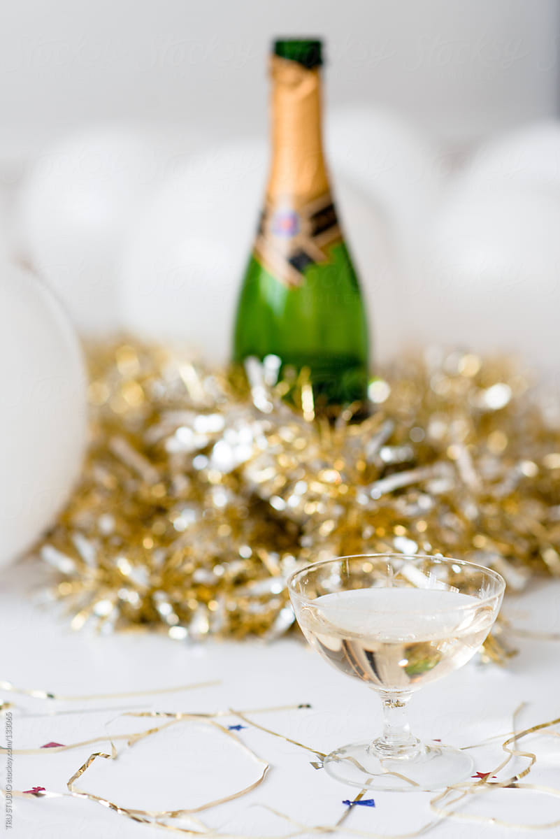 Champagne glass in front of bottle at a party with balloons and confetti and gold streamers