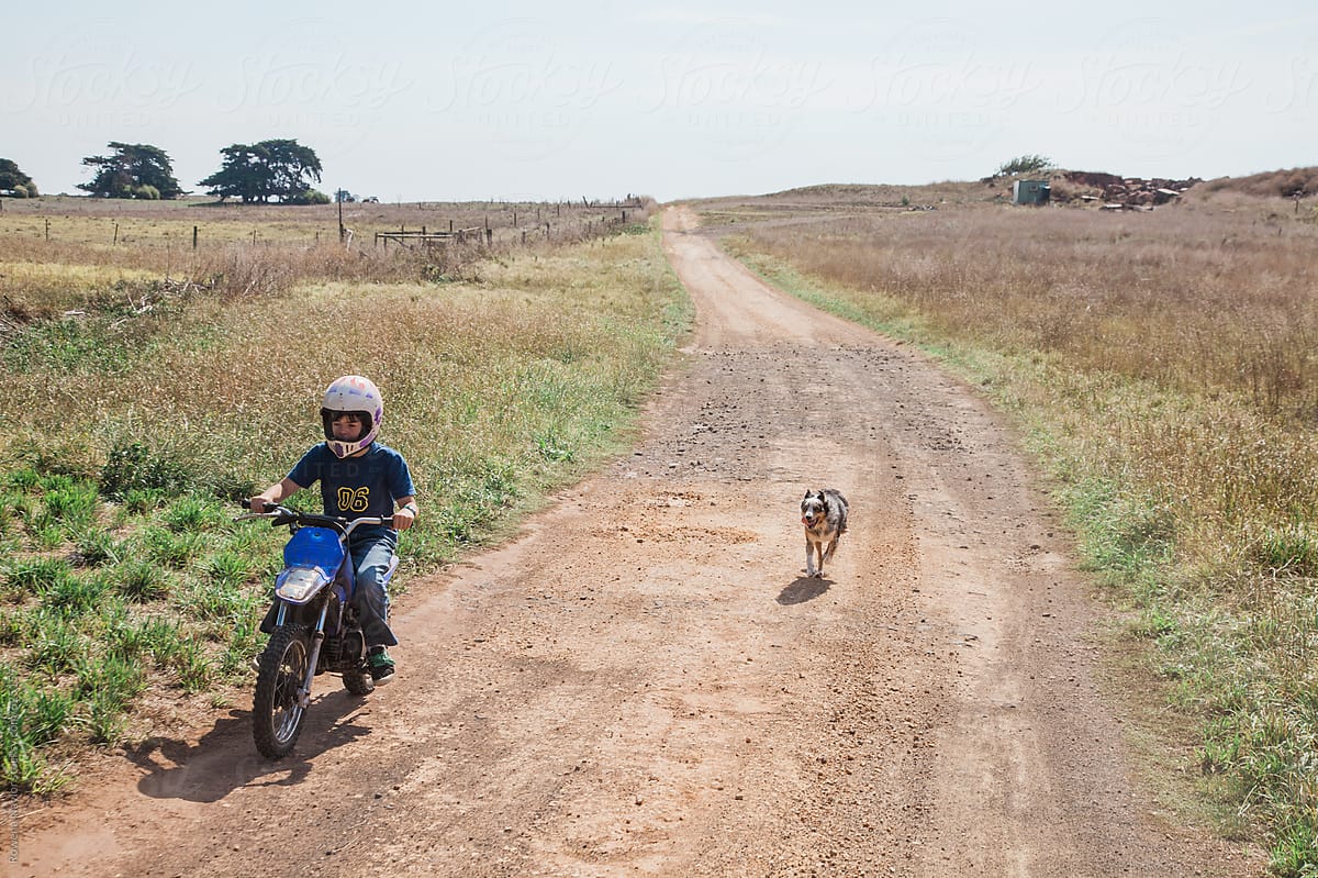Farmkid riding his trail bike on the farm with his dog alongside