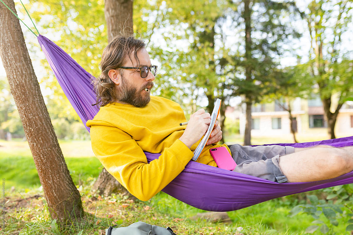 man writing in a notebook while sitting in a hammock