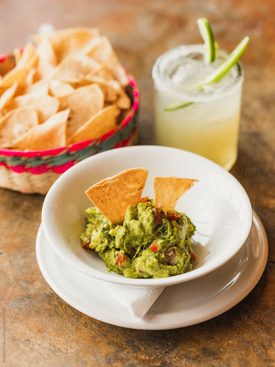 A basket of nachos or tortilla chips with guacamole and a margarita.