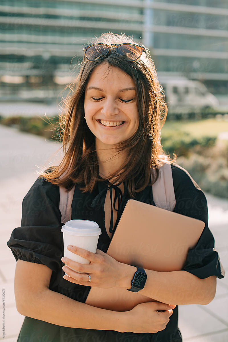 Smiling student with laptop and a cup of coffee to go