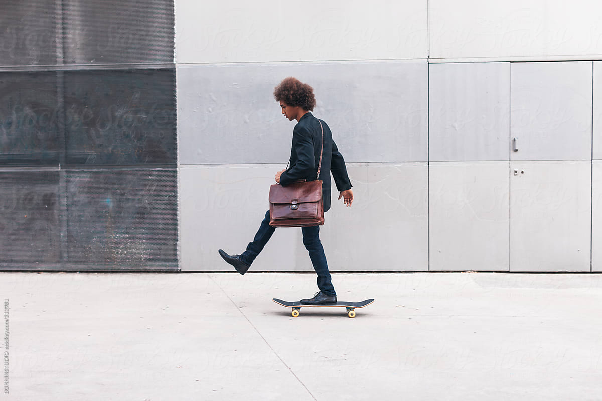 Modern afro businessman go to work on a skateboard. Ecological concept.