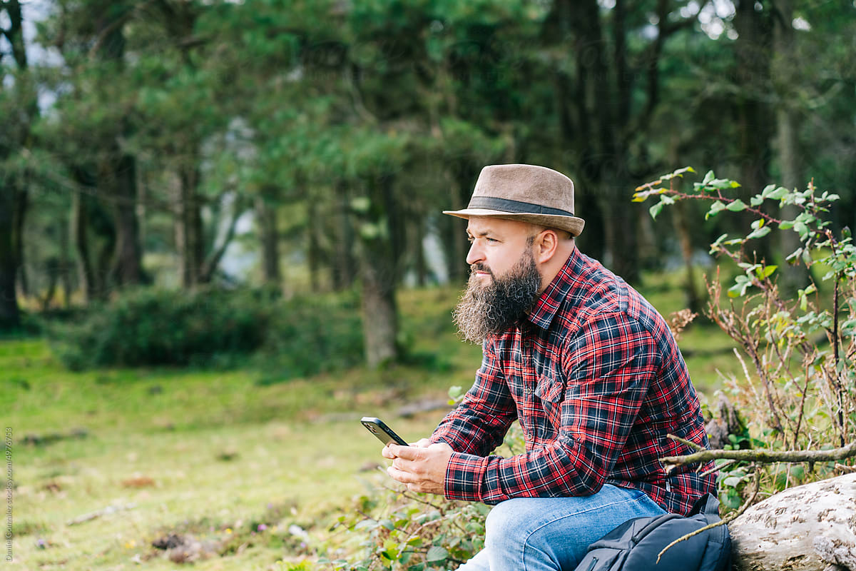 Pensive man using smartphone in forest