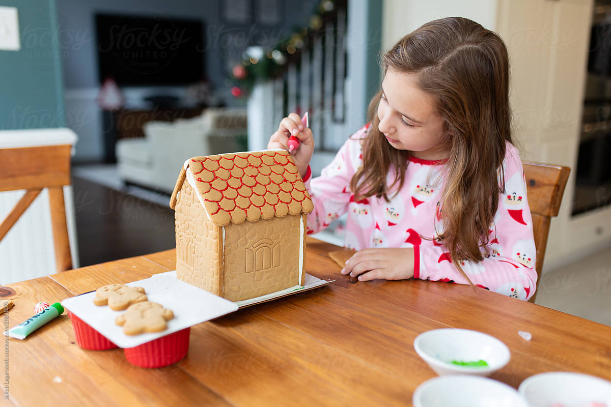 Cute young girl in Santa Claus pajama making decorating a gingerbread house