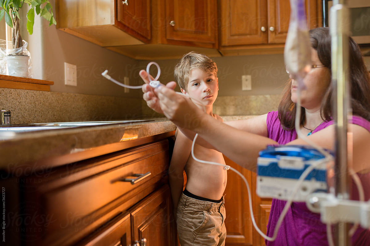 Woman prepares gastric feeding tube pump at home while son watches