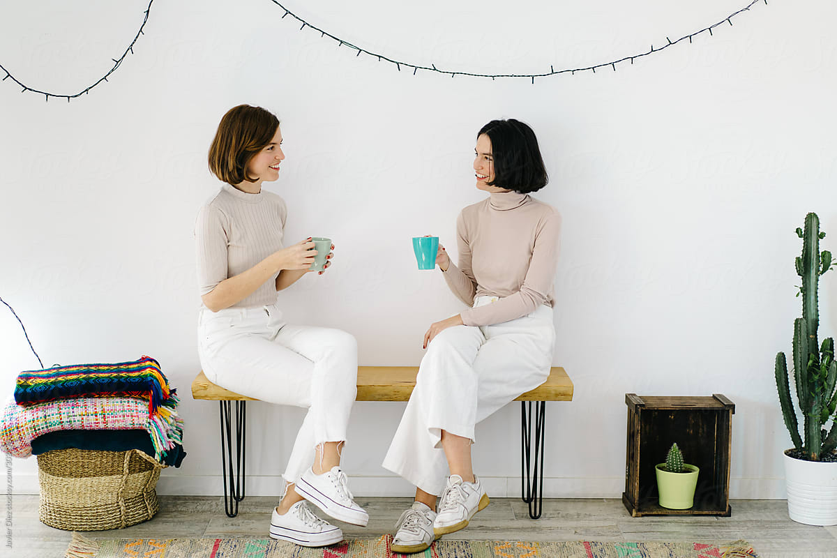 Cheerful sisters drinking hot beverage and chatting