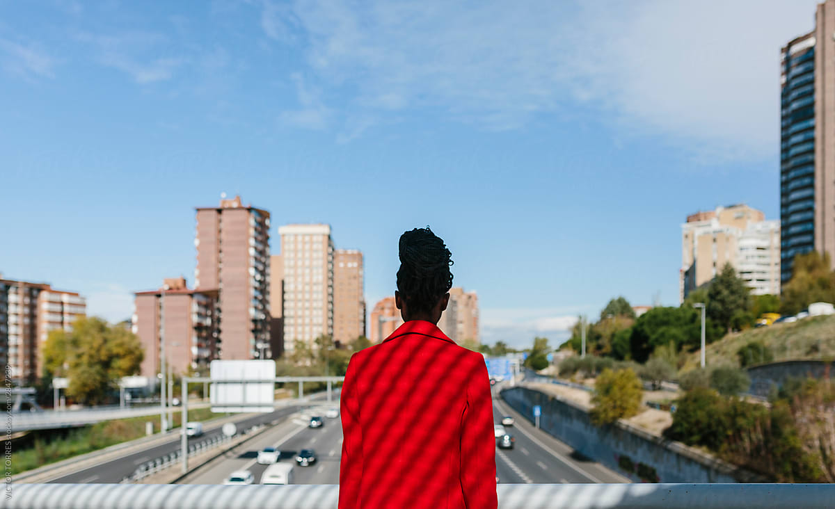 Calm black woman in red jacket looking at city