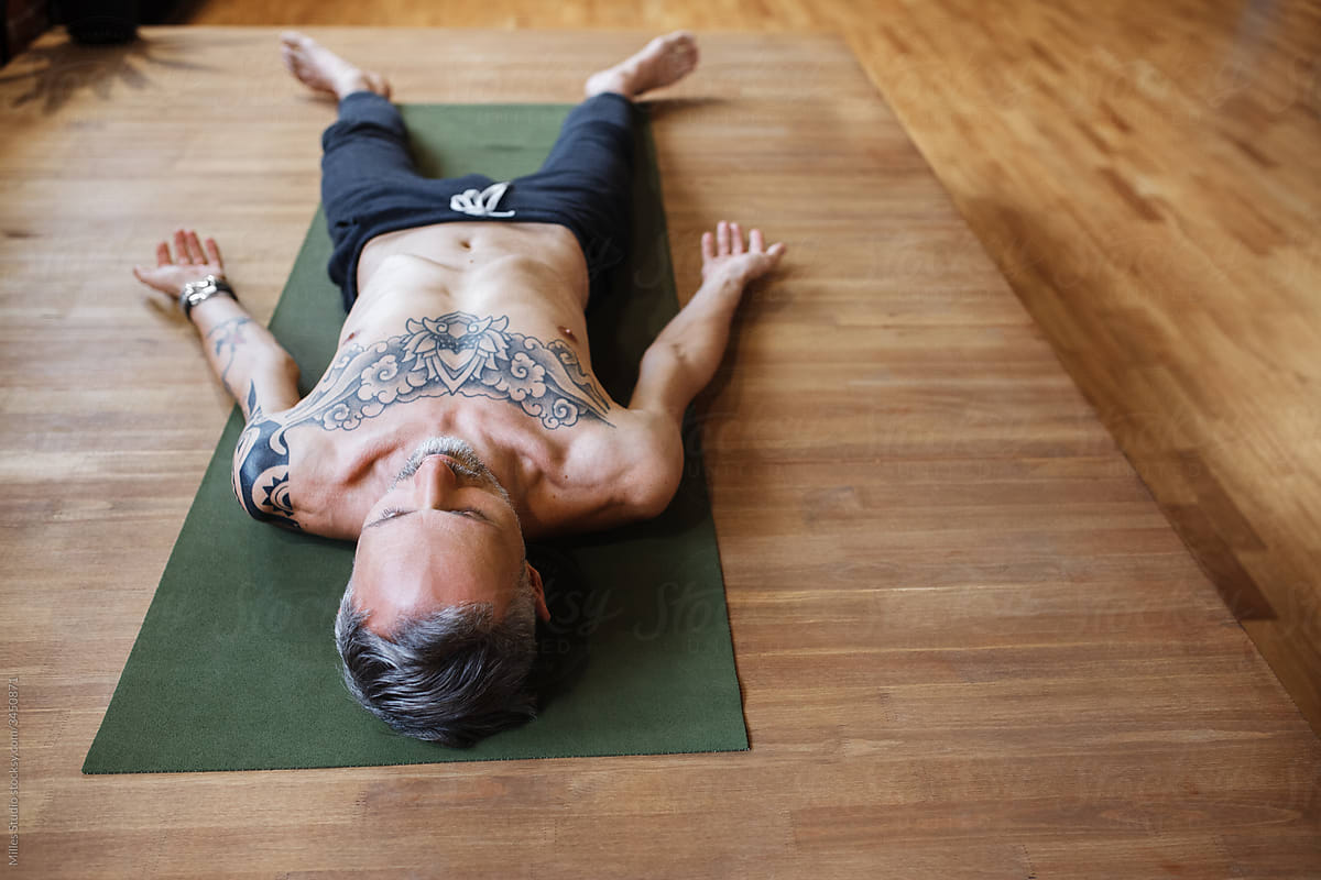 Tattooed man relaxing on floor during yoga lesson