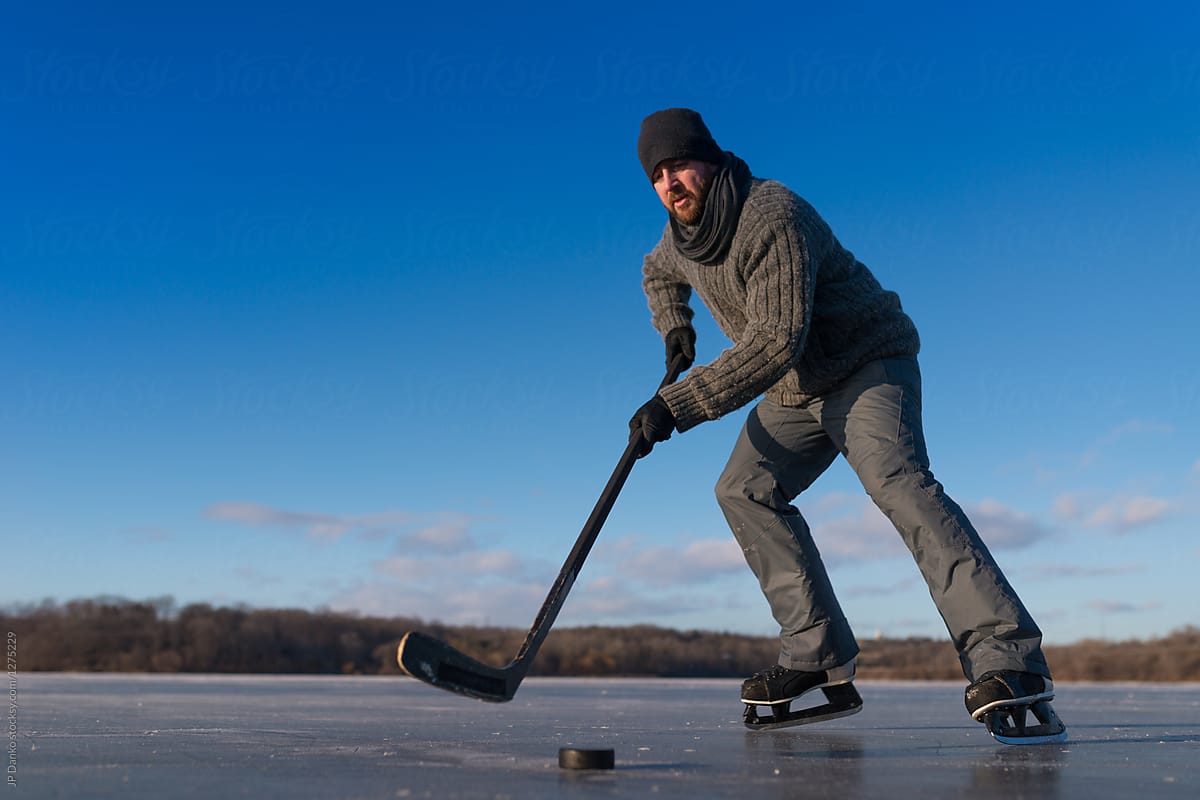 Man Skating With Puck Outdoors Playing Ice Hockey on Frozen Pond in Winter