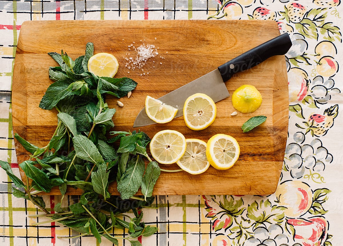 A knife rests on a cutting board with cut lemons and fresh mint.