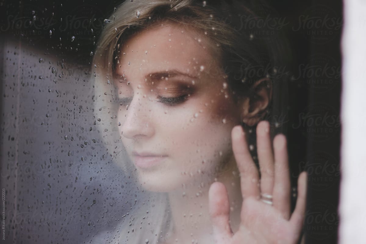 Beautiful young  woman standing at the window watching the rain