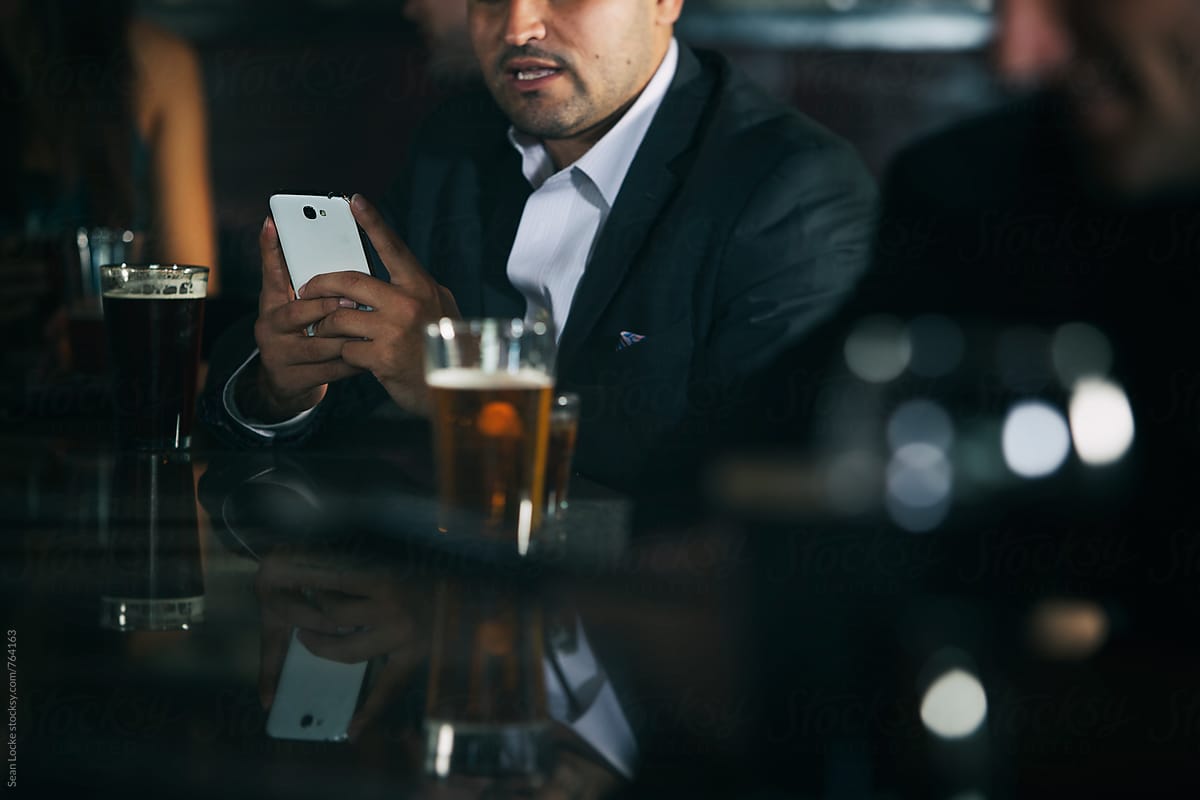 Bar: Businessman Checks Texts While Sitting At Bar With Friend