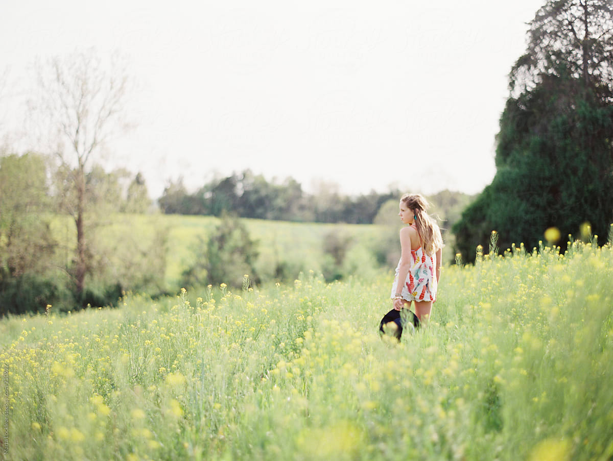 Girl In A Yellow Flower Field Looking Out Into The Distance Of The