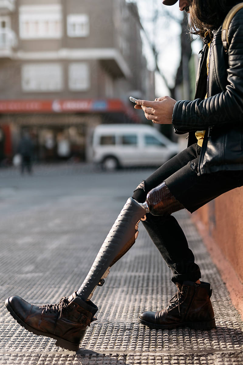 Trendy man with prosthesis using smartphone on street